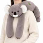 Szara koala przewieszona przez ramię dorosłej osoby, długie łapy zwisają z przodu, jasne tło, kadr od ramienia do pasa