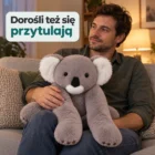 Mężczyzna po pracy w koszuli siedzi na kanapie z szarą koalą na kolanach, swobodny kadr
